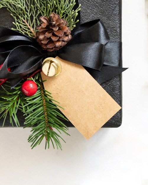 Regalo negro con etiqueta de regalo vertical de Navidad ramas de abeto conos de pino y decoraciones navideñas