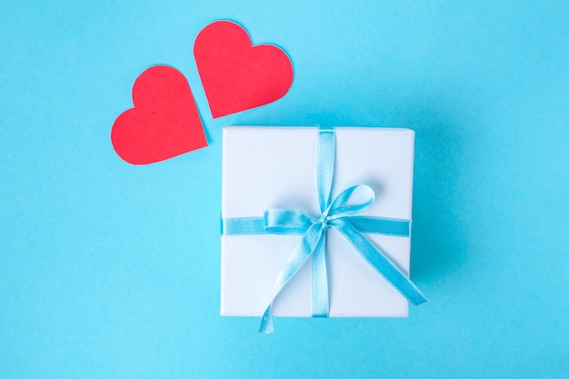 Regalo, pequeña caja atada con una cinta de raso azul y corazones rojos. Concepto de regalo. Sorpresas y regalos para los seres queridos. Felicidades por las vacaciones