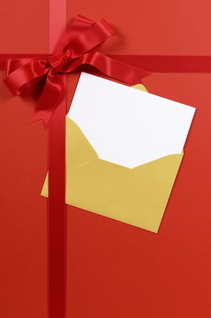 Regalo rojo con sobre de oro y tarjeta de invitación o saludos en blanco.