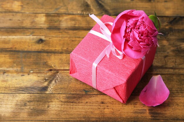 Regalo rosa con lazo y flor en primer plano de la mesa de madera