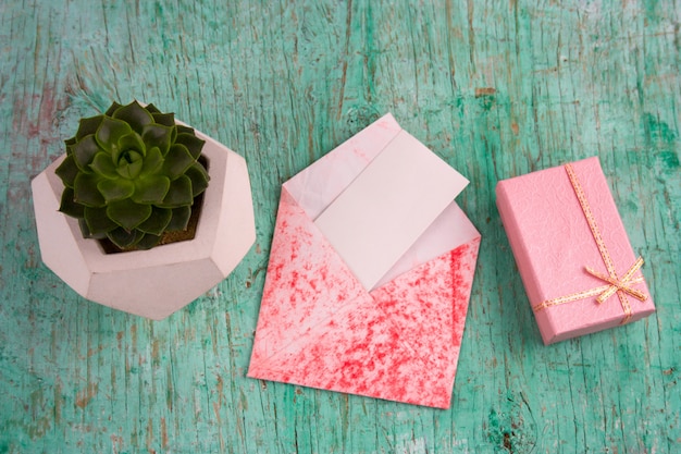 Regalo rosa, maceta suculenta y sobre con papel blanco en blanco simulado fondo de madera en mal estado