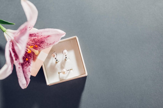 Regalo de San Valentín Conjunto de joyas de perlas en caja de regalo rosa con flores Pendientes y anillo con lirio sobre fondo gris Espacio de copia