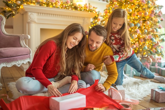 Regalos de año nuevo. Familia joven sentada en el suelo y empacando regalos de año nuevo