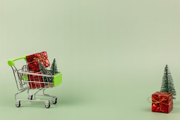 Regalos y un árbol de Navidad en un carrito de compras sobre un fondo verde.