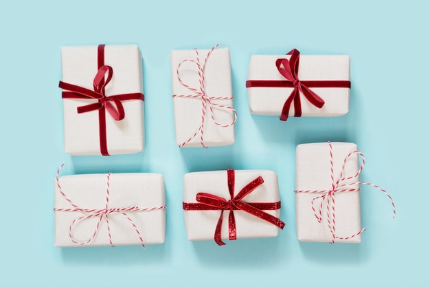Los regalos blancos de Navidad se envuelven en papel decorativo con lazo rojo sobre fondo azul.