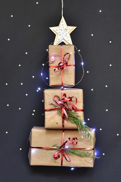 Regalos dispuestos junto a un árbol de Navidad y brillos esparcidos con estrellas sobre un fondo oscuro con luces.