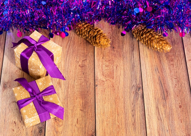 Los regalos se envasan en papel kraft y se atan con una cinta de raso con juguetes navideños y oropel morado sobre un fondo de madera Decoración para el árbol de Navidad