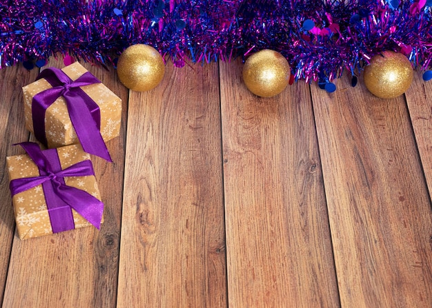 Los regalos se envasan en papel kraft y se atan con una cinta de raso con juguetes navideños y oropel morado sobre un fondo de madera Decoración para el árbol de Navidad