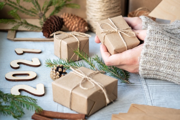 Regalos hechos de papel Kraft, ramas de árboles de Navidad, números de madera 2021, conos, ambiente festivo, primer plano. Preparación para el nuevo año, envoltura de regalos, materiales naturales.