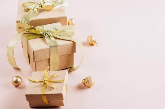 Regalos de moda o cajas de regalos con lazos dorados y bolas sobre fondo pastel en polvo Composición Navidad Enfoque selectivo con espacio de copia