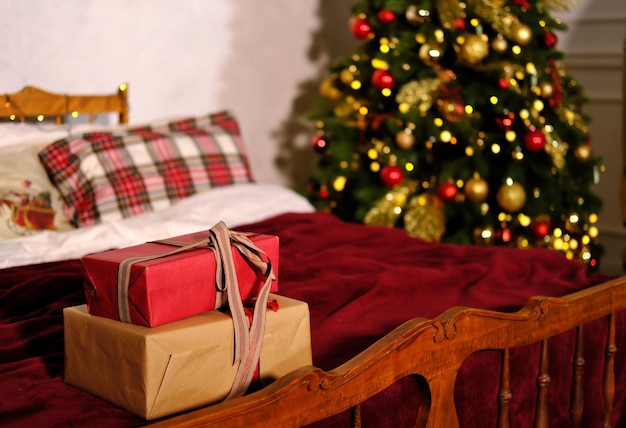 Los regalos de Navidad atados con una cinta yacen en la cama con el telón de fondo del árbol de Navidad