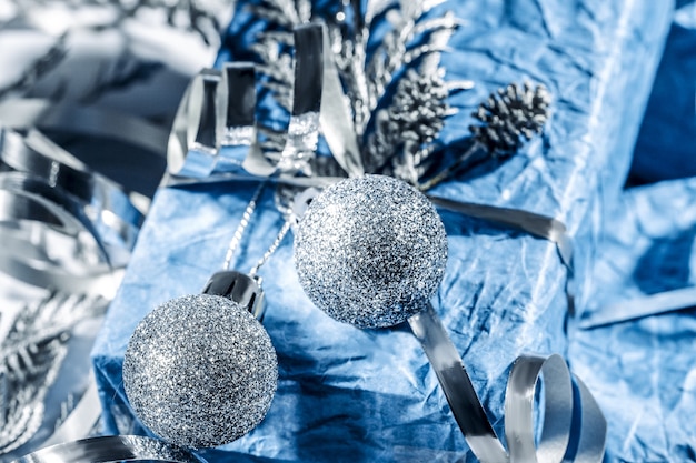 Regalos de Navidad con caja de regalo en color azul plateado decorado con piñas y ramitas sobre fondo blanco, preparación para las vacaciones. Regalos de Navidad y Año Nuevo. Hecho a mano. Enfoque selectivo.