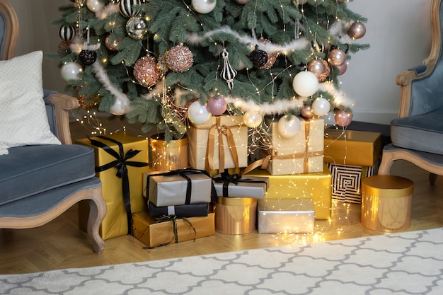 Regalos de Navidad cerca del árbol de Navidad con guirnaldas de luces brillantes en el piso de la sala de estar