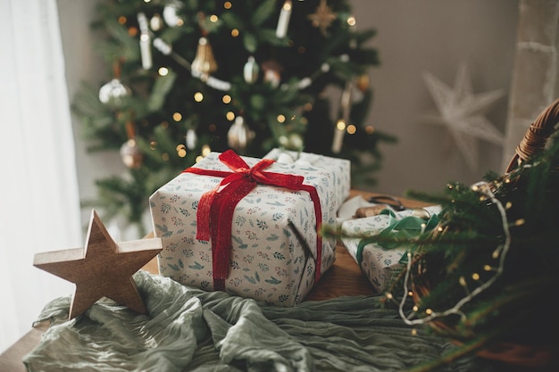 Regalos de Navidad envueltos con estilo cesta rústica con ramas de abeto y decoraciones modernas contra el árbol decorado festivo en la habitación escandinava Feliz Navidad y felices fiestas