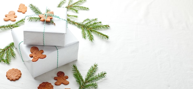 Regalos de Navidad envueltos en papel blanco y decorados con ramitas de abeto y galletas de jengibre sobre un fondo de tela