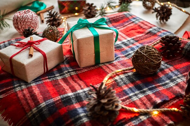 Regalos de Navidad en el fondo de una tela escocesa a cuadros de lana roja con guirnaldas de conos y ramas de abeto