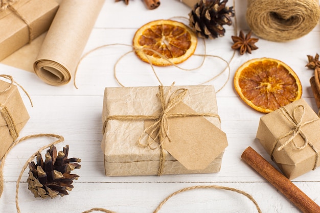 Regalos de papel artesanal, naranja seca, canela, piñas, anís en una mesa blanca