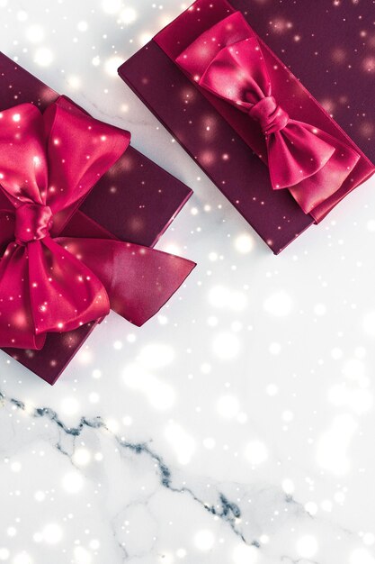 Regalos de vacaciones de invierno con lazo de seda de cereza y nieve brillante sobre fondo de mármol congelado Sorpresa de regalos de Navidad