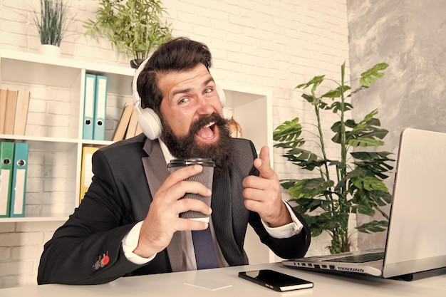 Regelmäßiger Morgen im Büro Motivationsmusik Viel Spaß beim Singen Hobby Mann Büroangestellter hört Musik Kopfhörer Stressresistenzkonzept Manager entspannt sich bei Lieblingsmusik und Tasse Kaffee