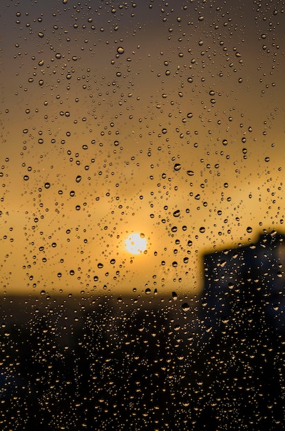 Regen außerhalb Fenster auf Hintergrund des Sonnenuntergangs. Bei Regen fällt Regen auf Glas. Sonnenuntergang außerhalb des Fensters während des Regens. Helle Textur von Wassertropfen