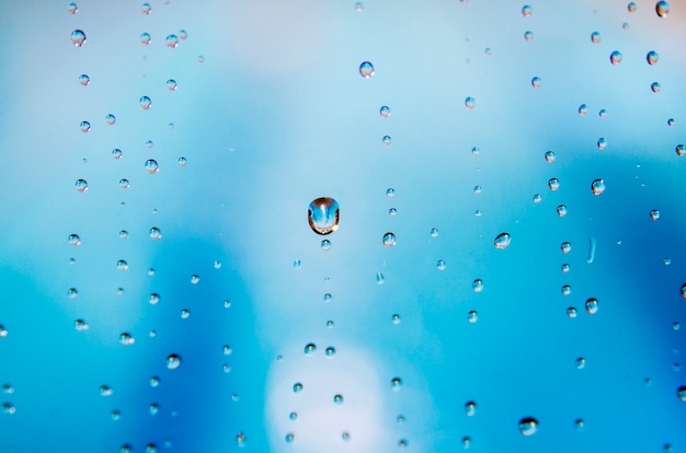 Regen fällt auf Fensterglas mit Unschärfehintergrund des blauen Himmels.