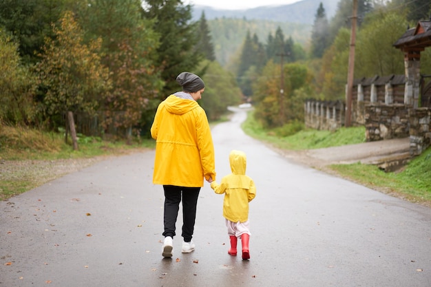 Regentag Mutter und kleine Tochter, die nach dem Regen spazieren gehen, kleideten gelben Regenmantel an