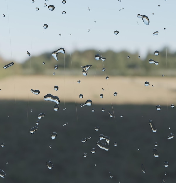 Regentropfen auf einem Autofenster mit einem Feld im Hintergrund