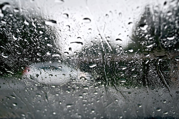 Regentropfen auf einem Glasfenster mit verschwommenen Bäumen, Straße und weißem Auto
