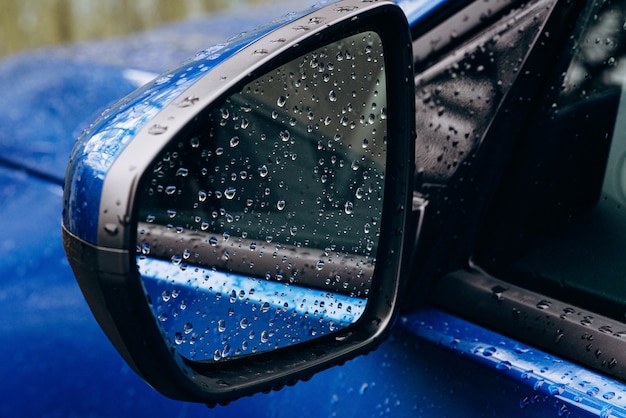 Regentropfen auf einem Spiegel eines blauen Autos. Herbst. Weicher selektiver Fokus.