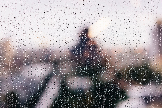 Regentropfen auf Fensterglas in der goldenen Stunde mit verschwommenen Hochhäusern im Hintergrund.