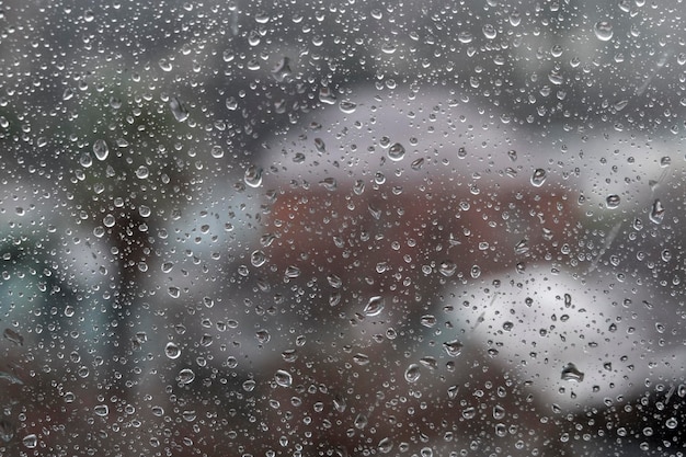 Regentropfen auf Fensterglasoberfläche mit bewölktem Hintergrund Natürliches Muster von Regentropfen