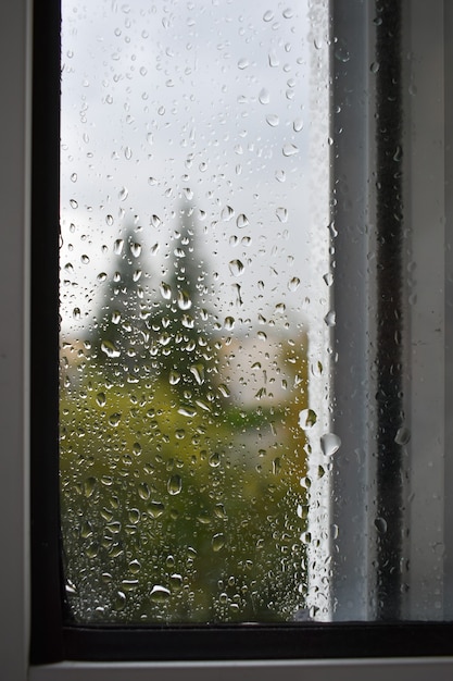 Regentropfen auf Fensterscheibe. Bewölktes Herbstwetter durch Glas. Verschwommenes Herbststadtbild.