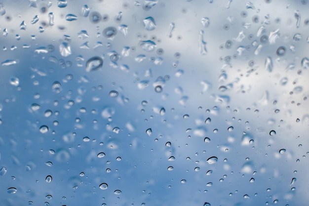 Regentropfen auf Fensterscheibe. Tau- oder Kondensationsbeschaffenheit am Fenster gegen blauen Himmel. Selektiver Fokus auf Regentropfen.