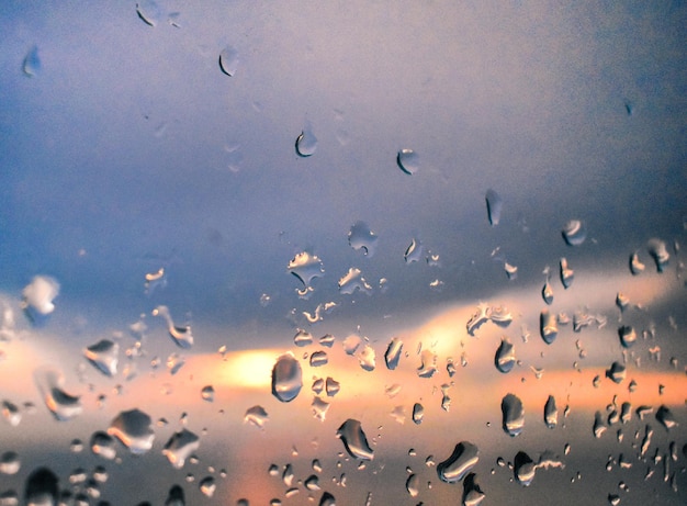 Regentropfen auf Glas gegen den Himmel und Sonnenuntergang