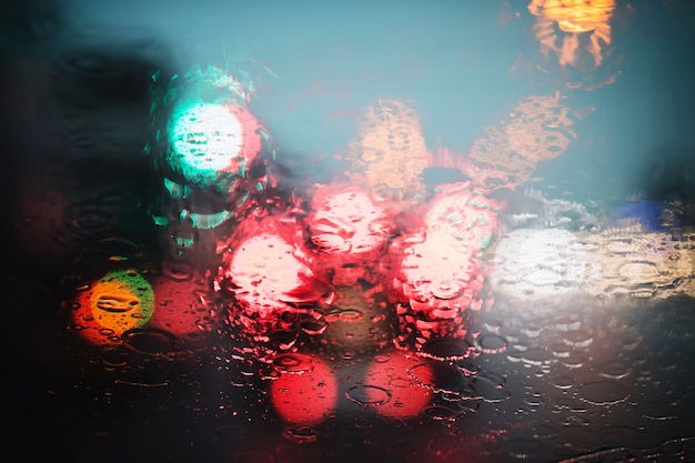 Regentropfen Nieselregen auf der Glaswindschutzscheibe in der Nacht. Straße bei starkem Regen. Bokeh-Rücklicht. Weicher Fokus. Bitte fahren Sie vorsichtig, rutschige Straße. Weicher Fokus. Stau Auto.