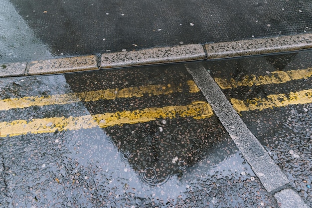 Regentropfen plätschern in einer Pfütze mit Reflexionen auf der Straße in London