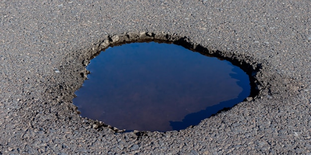 Regenwasser sammelt sich in einer Pfütze, was den verschlechterten Zustand der Straße noch verstärkt