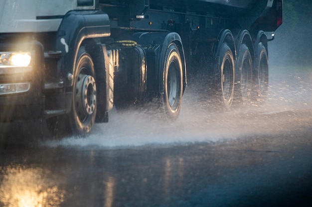 Regenwasserspritzer fließen von den Rädern schwerer Lastwagen, die sich schnell in der Tageslichtstadt mit selektivem Fokus bewegen