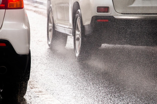 Regenwasserspritzer fließen von den Rädern weißer Autos, die sich schnell in der Tageslichtstadt mit selektivem Fokus bewegen