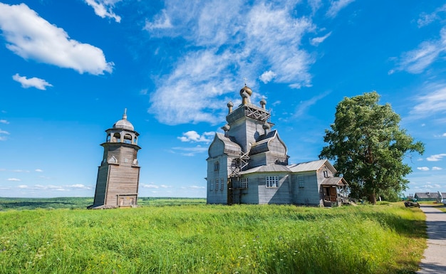 Região de Arkhangelsk, a aldeia de Turchasovo, perto do rio Onega, a antiga Igreja de madeira da Transfiguração de 1786 e a torre do sino de 1793 contra o céu azul no verão