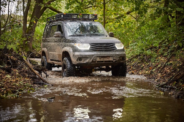 Região de Moscou Rússia 28092018 Viajando offroad em um caminhão UAZ Patriot preto O carro está dirigindo ao longo de um riacho na floresta