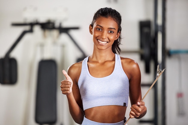 Regístrate Solo te arrepentirás si no lo haces Foto de una joven deportista sosteniendo un portapapeles y mostrando los pulgares hacia arriba en el gimnasio