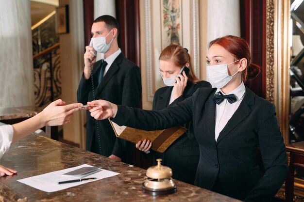 Registro en el hotel. recepcionista en el mostrador del hotel con máscaras médicas como precaución contra el virus. Mujer joven en un viaje de negocios haciendo el check-in en el hotel