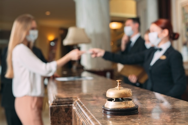 Registro en el hotel. recepcionista en el mostrador del hotel con máscaras médicas como precaución contra el virus. Mujer joven en un viaje de negocios haciendo check-in en el hotel