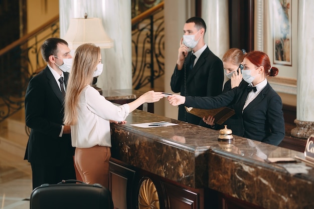 Registro en el hotel. recepcionista en el mostrador del hotel con máscaras médicas como precaución contra el virus. Mujer joven en un viaje de negocios haciendo check-in en el hotel