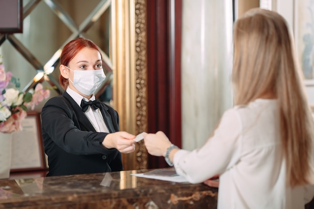 Registro en el hotel. recepcionista en el mostrador del hotel con máscaras médicas como precaución contra el virus. Mujer joven en un viaje de negocios haciendo check-in en el hotel