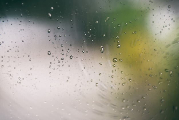 Regnen Sie Tropfen auf Glasfensterglas des regnerischen Tages mit Wassertropfen und grünem Unschärfehintergrund der Natur