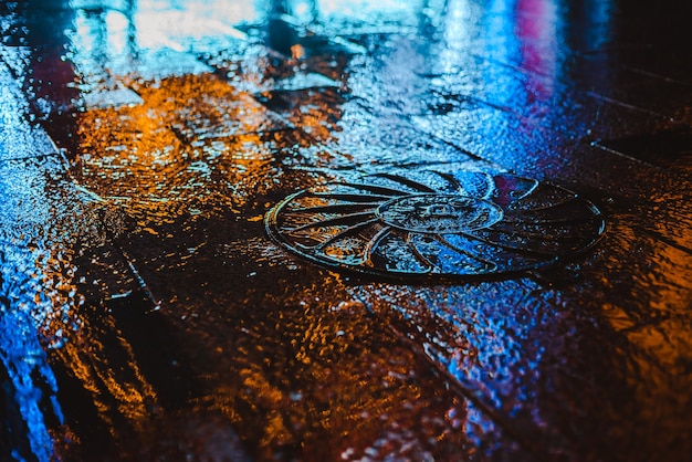 Regnerische Nacht in einer Großstadt, Reflexion der bunten Stadtlichter auf der nassen Straßenoberfläche.