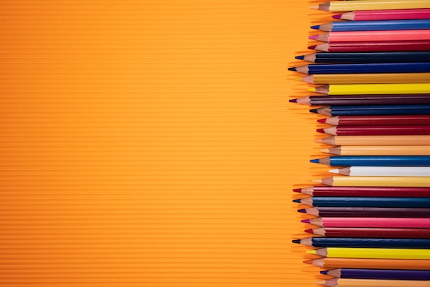 Regresar al concepto de escuela. Lápices de colores sobre fondo naranja.