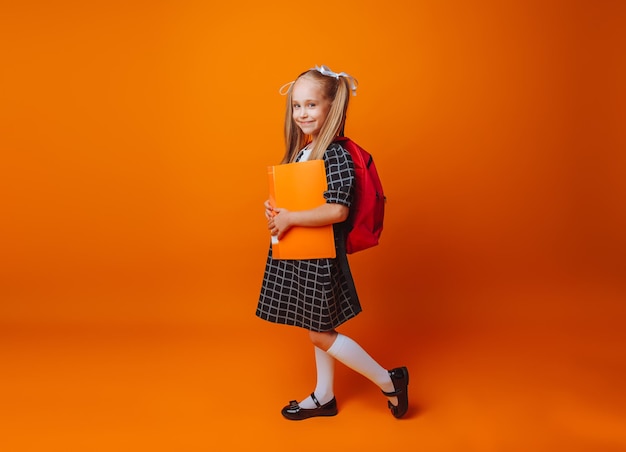 Regreso a la escuela Una colegiala con una mochila escolar sobre un fondo de estudio amarillo aislado una niña sostiene una carpeta y una mochila